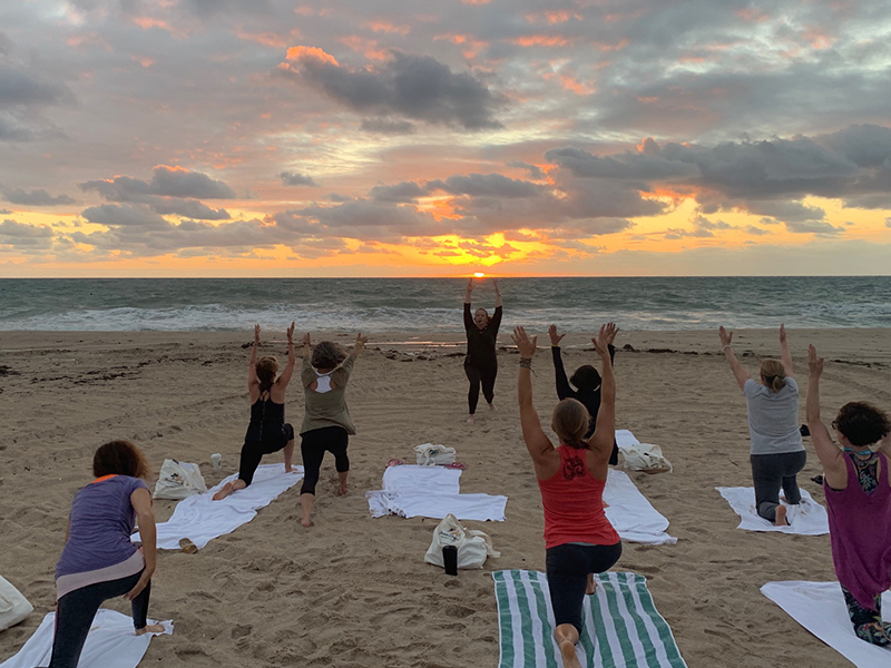 View of yoga class on the beach doing a lunge with their arms up