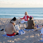 View of yoga instructor speaking to her class on the beach.